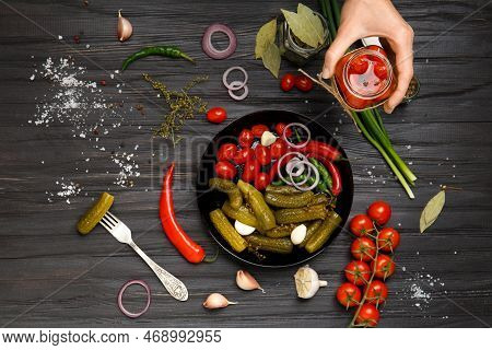 A Plate With Canned Vegetables And A Jar Of Pickled Cherry Tomatoes In Hands On A Dark Background. P