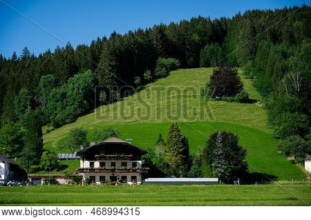 Panoramic View Of Beautiful Mountain Landscape, Green Austrian Village In The Alps, Mountains Surrou
