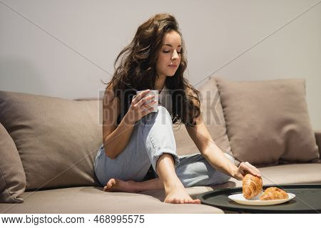 Beautiful Happy Lady In Casual Clothes Sitting On Couch Indoors Holding In Hands Cup Of Hot Drink An