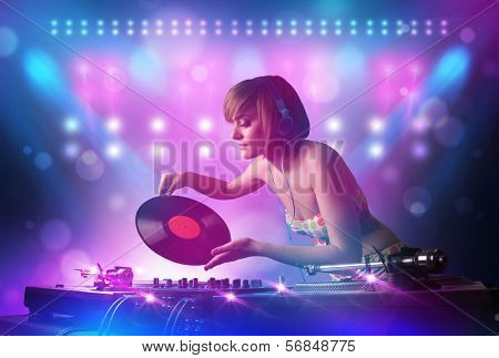 Pretty young disc jockey mixing music on turntables on stage with lights and stroboscopes