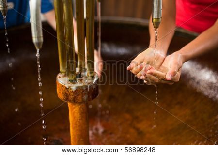 People filling up their hands with healthy mineral water from a wellspring in a spa (shallow DOF)