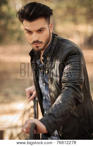 young fashion man leaning on a bech in the park while looking away from the camera.