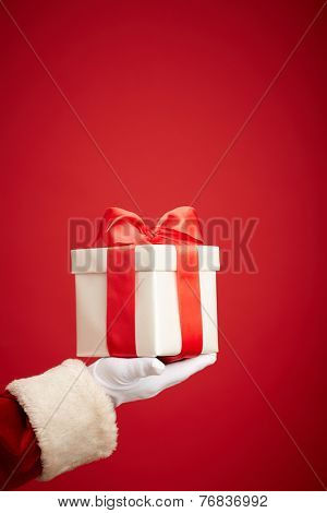 Santa Claus gloved hand holding giftbox with red bow