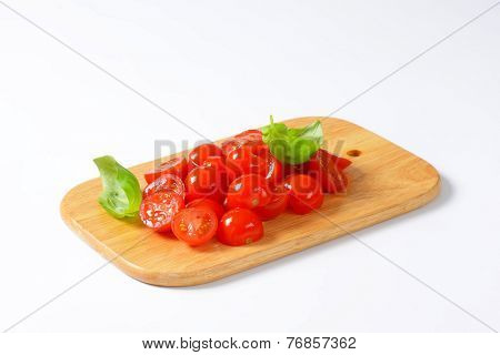 halved cherry tomatoes decorated with fresh basil, on the wooden cutting board