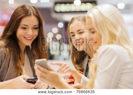 sale, consumerism, technology and people concept - happy young women with smartphones and tablet pc in mall or city