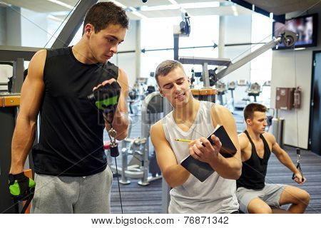 sport, fitness, lifestyle and people concept - men with clipboard taking notes and exercising on gym machine