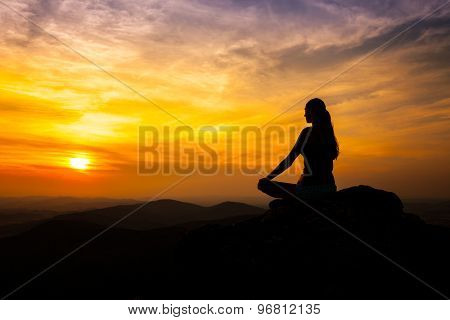 Yoga practicioner sitting on rock during the sunset meditation