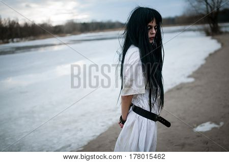 Crazy Young Woman Stands On Sand Along Lake. Side View.