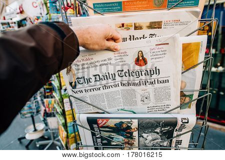 PARIS FRANCE - MAR 23 2017: Man purchases The Daily Telegraph with title New Terror ban of iPad - newspaper from press kiosk newsstand featuring headlines