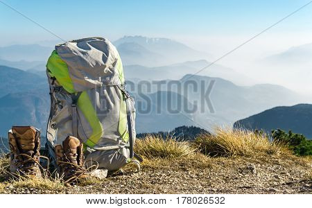 Hiking equipment. Backpack and boots on top of the mountain. Beautiful view to mountain ranges and fog filled valleys.