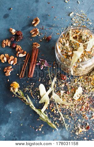 Cinnamon sticks nuts and a herb collection scattered on a blue table a glass jar with tea lime mint lemon balm chamomile. Daylight vertical image.