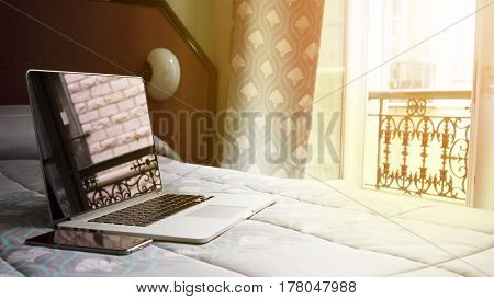 a laptop on the bed in the room in Paris writing fashion blog in Paris working at home or wathing movie on the bed. A silver laptop located on the bed near the window