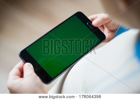 The child is holding a phone in his hand with a green screen for chroma keyer