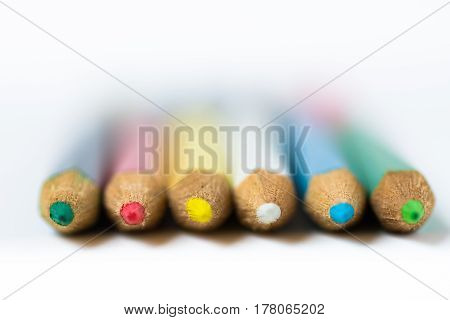 Row of colored crayons or pencils on white background macro closeup defocused abstract styled photo for product marketing social media education concept