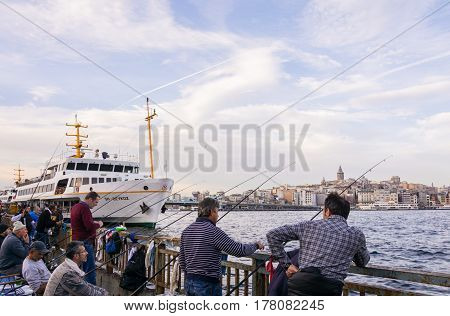 ISTANBUL, TURKEY - NOVEMBER 19, 2014: Turkish fishermen fishing on Iskele Yolu in Eminonu district in Istanbul Turkey with view over Bosporus Galata Tower and Galata Bridge