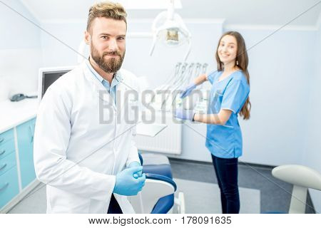 Handsome dentist with young female assistant in uniform prepairing for the job at the dental office
