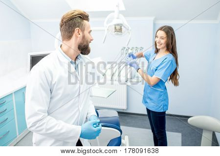 Handsome dentist with young female assistant in uniform prepairing for the job at the dental office