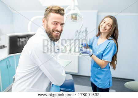 Handsome dentist with young female assistant in uniform prepairing for the job at the dental office