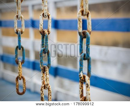 Rusty metal chain on a white and blue fence.