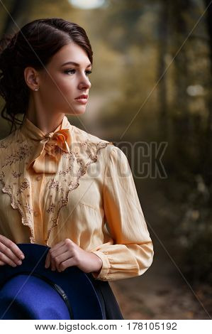 closeup outdoor fashion portrait of sensual stylish girl in vintage blouse. Young woman with romantic hairstyle and floppy hat in the forest. Beautiful brunette girl with brown eyes. Female retro look