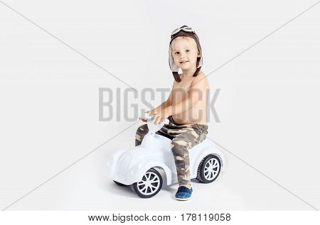Cute happy boy little child wearing vintage motorbike helmet with glasses smiling riding toy car isolated on white background copy space