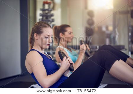 Pair of young adult women doing abdominal muscle Russian twist exercises while holding weights