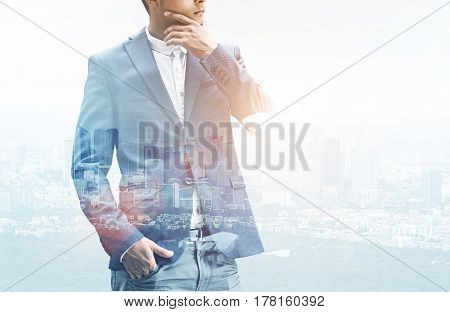 Close up of an unrecognizable businessman rubbing his chin while satanding against a city panorama. Double exposure