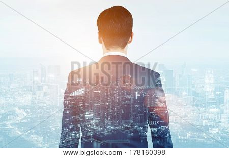Rear view of a businessman wearing a suit and glancing at a city panorma in the morning. Double exposure.
