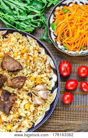 National Uzbek dish pilaf with meat garlic and red pepper on a traditional plate tomatoes carrots and herbs on a brown wooden table
