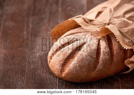 Loaf of rye bread in paper bag on wooden table. Bakery background. Decorative rope. Flour. Brown background. Tasty and appetizing.