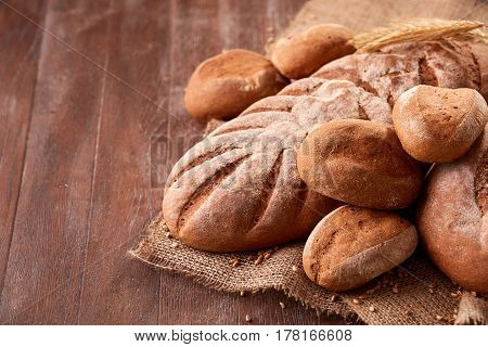 handmade tasty bread lying on burlap on the wooden table with flour, wheat and ears of wheat. Brown bread and rulls. Delicious food. Fresh baking. Tasty and appetizing.