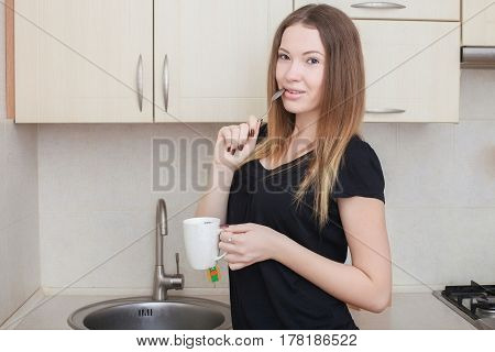 Beautiful young woman having morning coffee, relaxing hot drink, happy female holding cup of tea, pretty girl eating and drinking healthy food at home, health care and dieting concept.