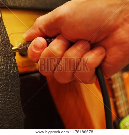 Hand inserts input jack to combo amplifier for guitar. Shallow depth of field low key close up.