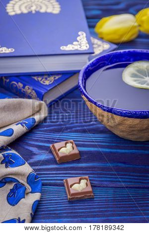 Lemon tea, books, milk chokolade and yellow tulips on a blue wooden background