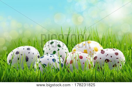 Easter egg background with coloured paint speckled easter eggs in long green grass with bright lights in blue sky