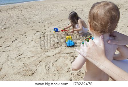 Mother applying sun cream to her baby while her daughter play on sand Huelva Spain