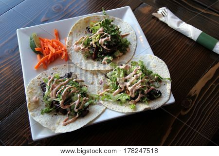 Large white plate with three tacos filled with rib-eye, drenched in 
a sweet-tangy bbq sauce for dinner in restaurant.