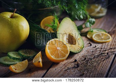 Background with assorted green vegetables: apple avocado cucumber lemon and detox water on rustic wooden table top. Healthy food detox dieting vegetarian and weightloss concept with copy space.