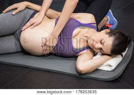 Trainer massaging pregnant woman on exercise mat