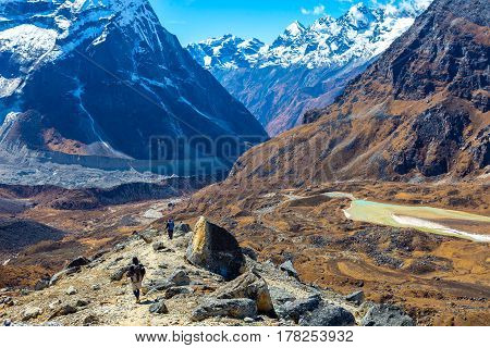 Mountain Valley View and Group of People walking on Trek carrying Backpacks using trekking Sticks dressed in alpine Jackets and hiking Pants