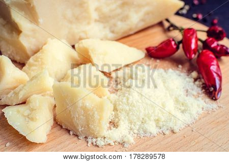 Grated Parmesan cheese with chili pepper on wooden chopping board on dark background. Tasty appetizers. Selective focus.