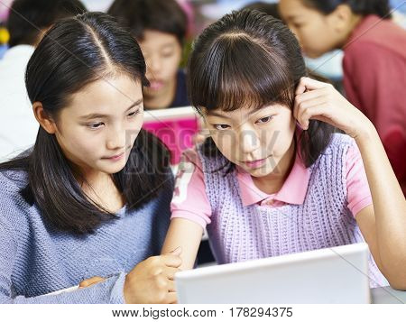 two asian elementary school girls looking at tablet computer thinking hard while working in groups.