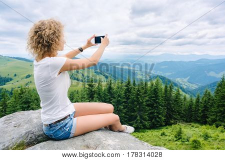 Beautiful woman hiker taking photo with cellphone on mountain top