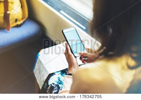 Enjoying travel. Young pretty woman traveling by train sitting near the window using smartphone and looking map. Tourist texting online message and plan route of railway railroad transport concept mock up
