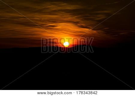 The sky is magenta and orange with alpenglow and clouds. Abstract red orange sky. Dramatic orange sky at the sunset background. The sundown behind hills. Dark in the evening.