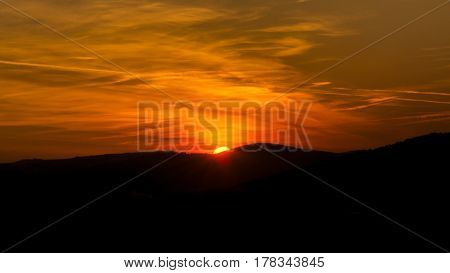 The sky is magenta and orange with alpenglow and clouds. Abstract red orange sky. Dramatic orange sky at the sunset background. The sundown behind hills.