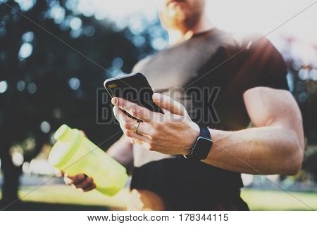 Smart workout concept.Young Muscular athlete checking training programm on smartphone application after perfect workout session at sunny morning.Blurred background