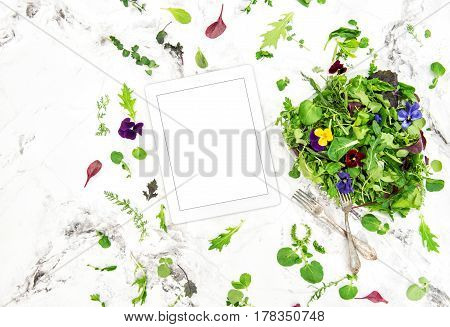 Food background tablet PC. Green salad with herbs and flowers. Healthy organic nutrition. Digital recipe book
