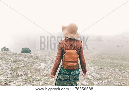 Boho woman wearing hat and leather jacket walking in mountains. Cold weather and fog. Spring or fall hiking. Wanderlust.