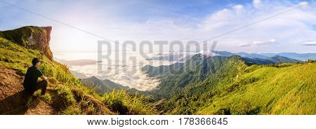 Panorama beautiful landscape nature Male tourist are watching the sunrise on peak mountain with sun cloud fog and bright sky in winter at Phu Chi Fa Forest Park famous attraction of Chiang Rai Province Thailand